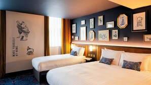 Una habitación de hotel con dos camas, un mural grande en la pared y varias fotografías enmarcadas.