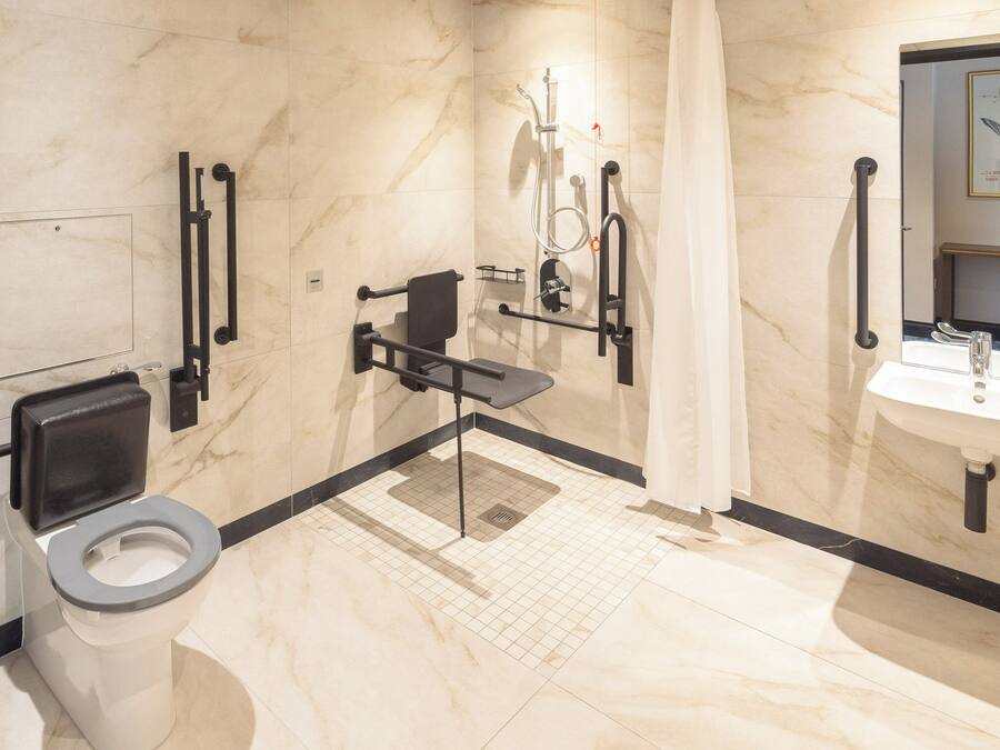 A modern bathroom with a toilet, grab bars, a shower, and a sink.