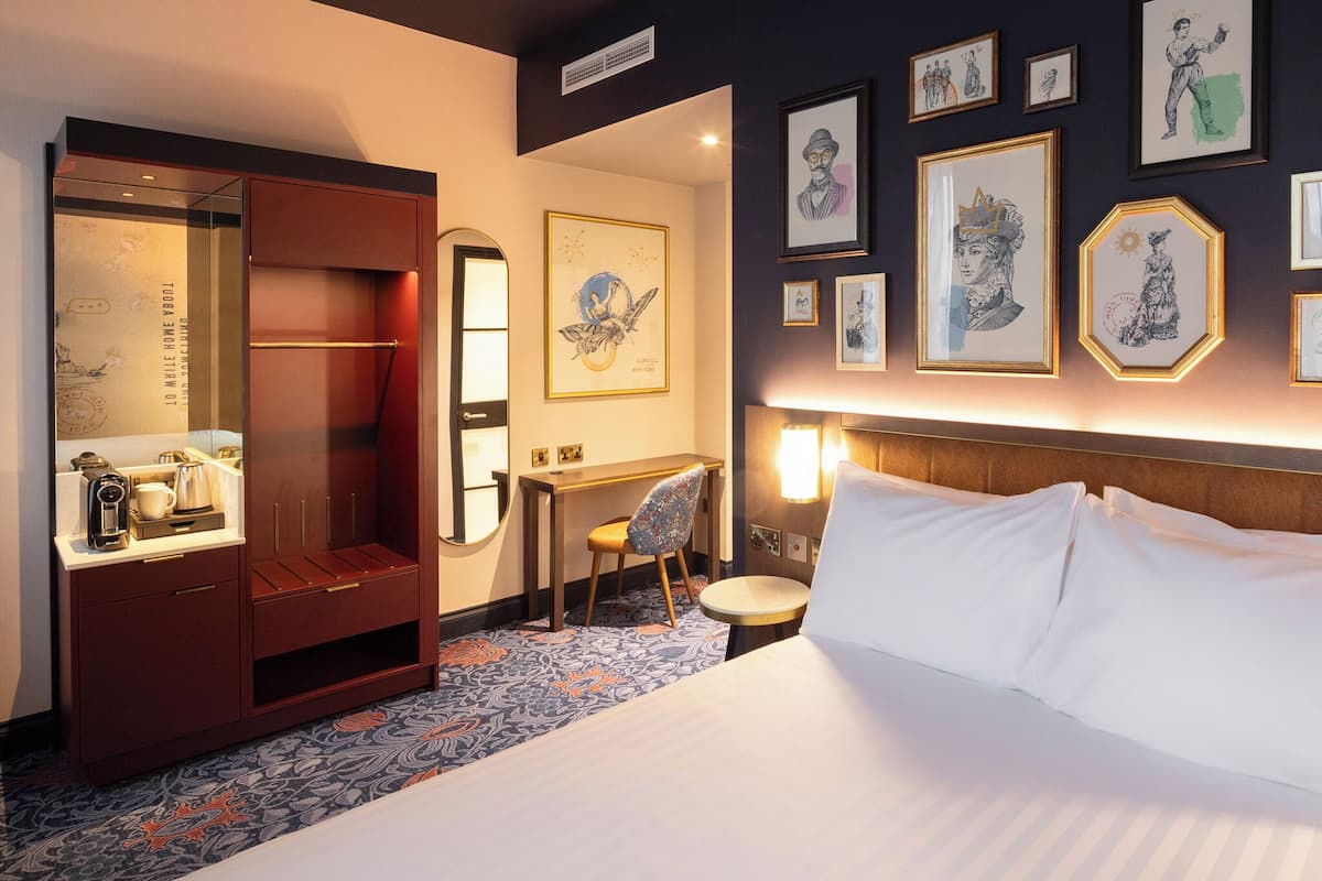 Une chambre d’hôtel équipée d’un lit, d’un bureau, d’une chaise, d’une armoire et de tableaux encadrés aux murs.