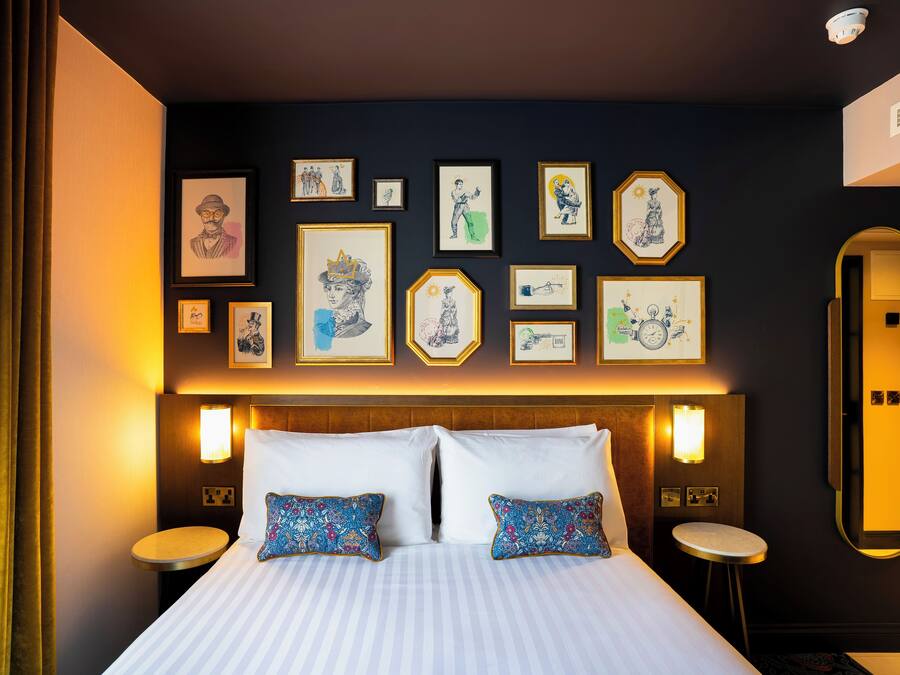 A hotel room with a large bed, two bedside tables, a wall-mounted mirror, and various framed artworks.