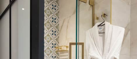 A modern bathroom with a glass-enclosed shower, a white robe hanging on a towel rack, and a patterned tile backsplash.