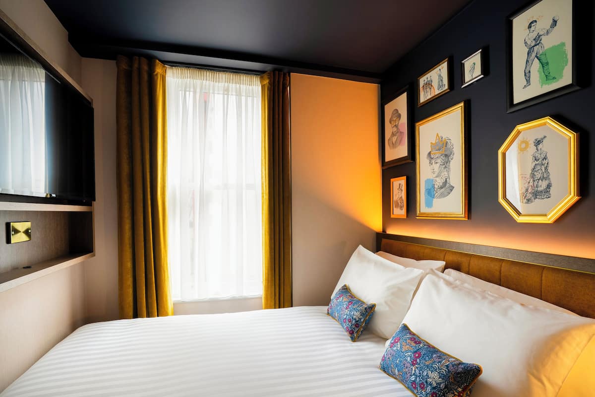 Une chambre d’hôtel avec un grand lit, un téléviseur fixé au mur et des œuvres d’art encadrées accrochées au mur.
