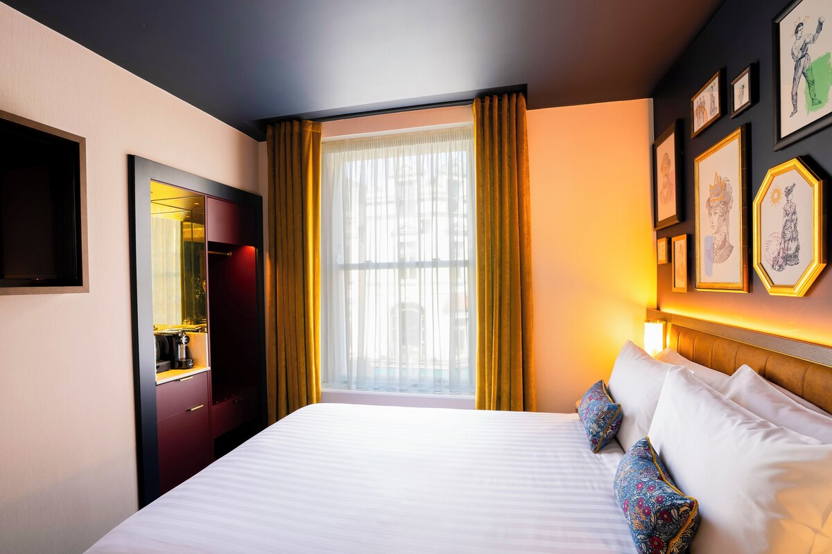 Una habitación de hotel con una cama grande, una ventana con cortinas, un armario y cuadros en la pared.