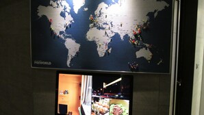 Un mapa mural del mundo con chinchetas y un televisor debajo que muestra una escena de restaurante.