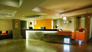 Zona de recepción de hotel con un mostrador, un sofá, un reloj y un jarrón decorativo.