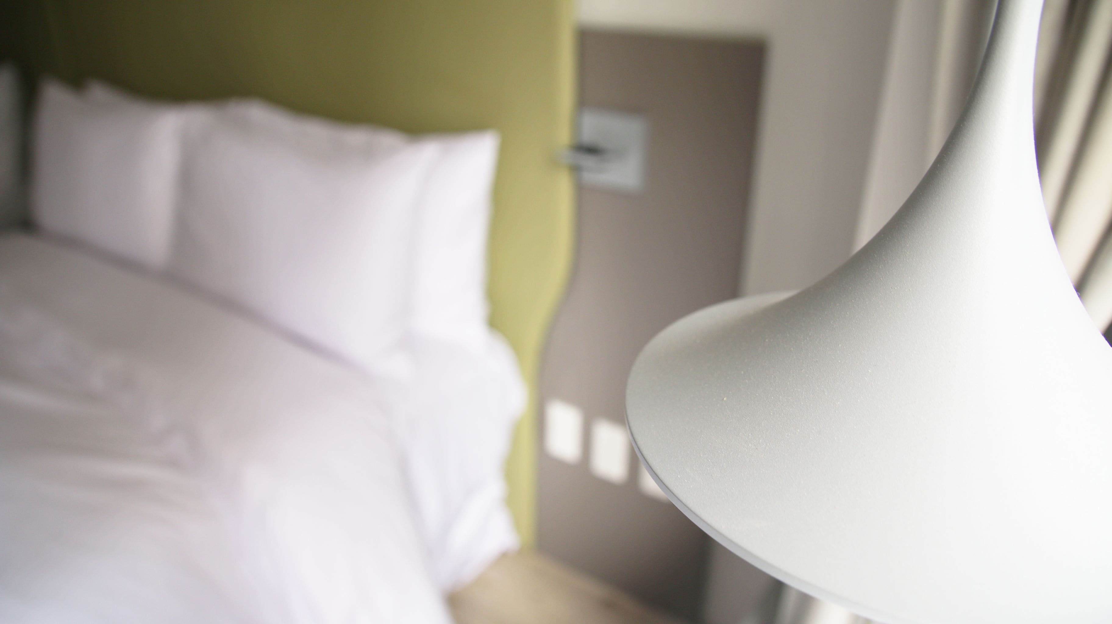 Een close-up van een witte lamp en een bed met witte lakens in een hotelkamer.