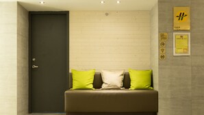 Un vestíbulo moderno con una puerta oscura, un sofá marrón con cojines verde y blanco, y una pared con varios letreros y un certificado enmarcado.