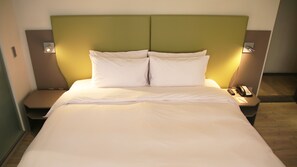 A hotel room with a bed, two bedside tables, a nightstand with a phone, and a wall-mounted light. - Horizon Inn (Taipei)