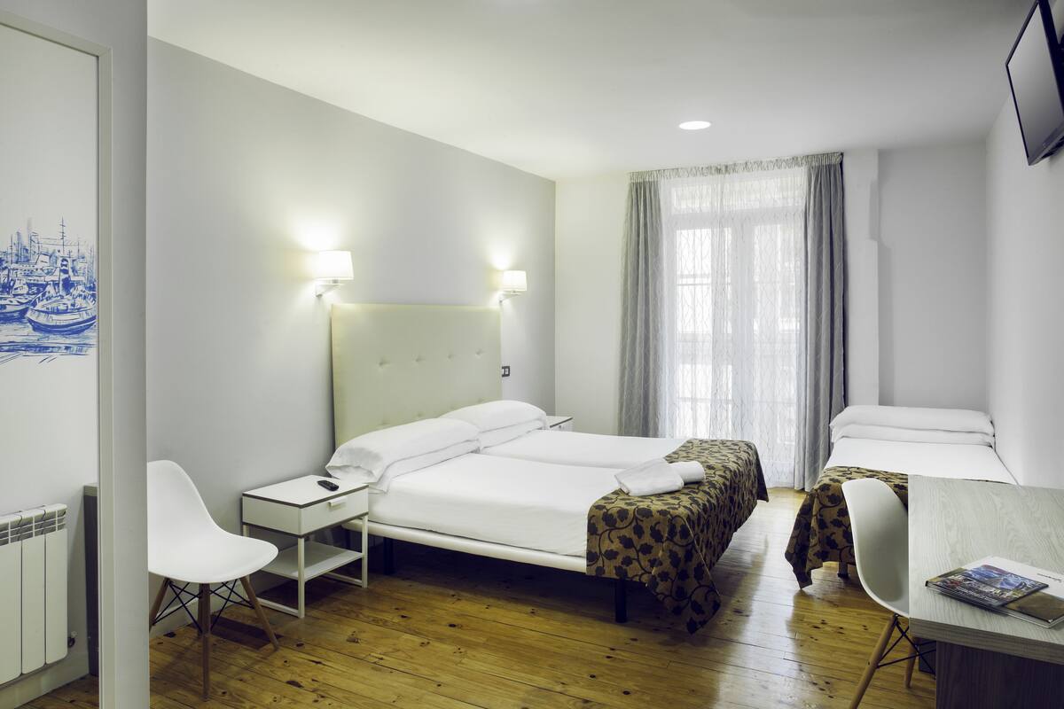 Une chambre d’hôtel comprenant un lit, une table de chevet, une lampe, une chaise et un bureau avec un magazine.