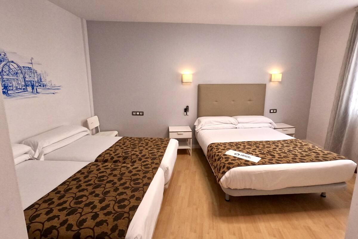 Une chambre d’hôtel avec deux lits, une table de chevet, une lampe fixée au mur et un tableau.