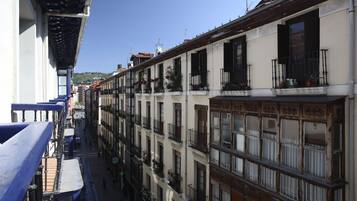 Una calle estrecha flanqueada por edificios de varios pisos con balcones, algunos con macetas.
