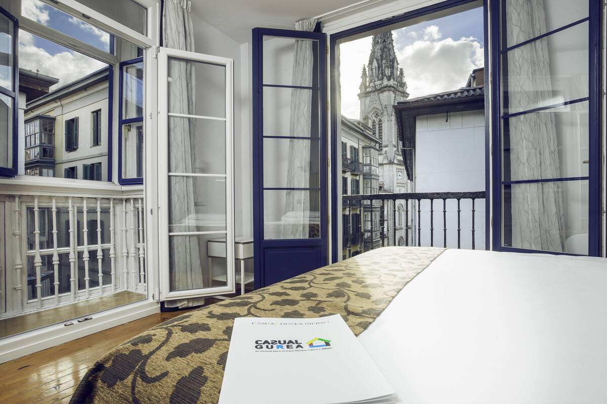 Une chambre d’hôtel avec vue sur un bâtiment historique, un tapis à motifs et une brochure posée sur le lit.