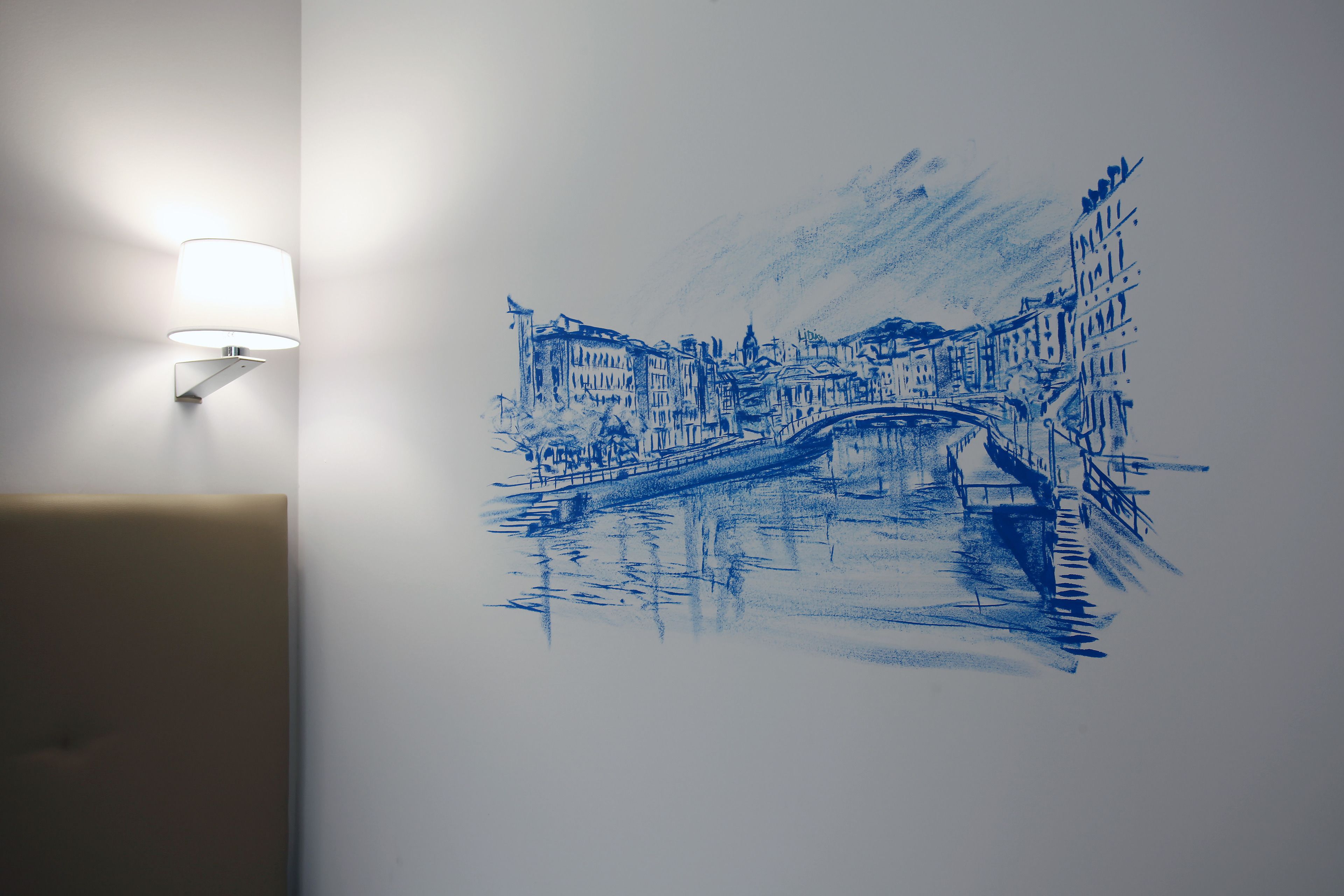 Una pared con un boceto azul de un puente y edificios, y una lámpara de pared.