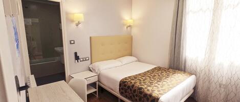 A hotel room with a bed, bedside table, and a desk.