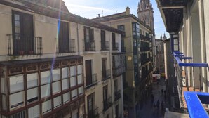 Una calle estrecha flanqueada por edificios, una aguja de iglesia a lo lejos y un toldo azul a la derecha.