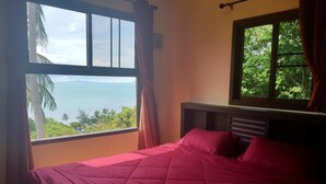 A room with a bed, a window with a view of the sea, and a curtain. - Moonstone Studio (Ko Pha-ngan)