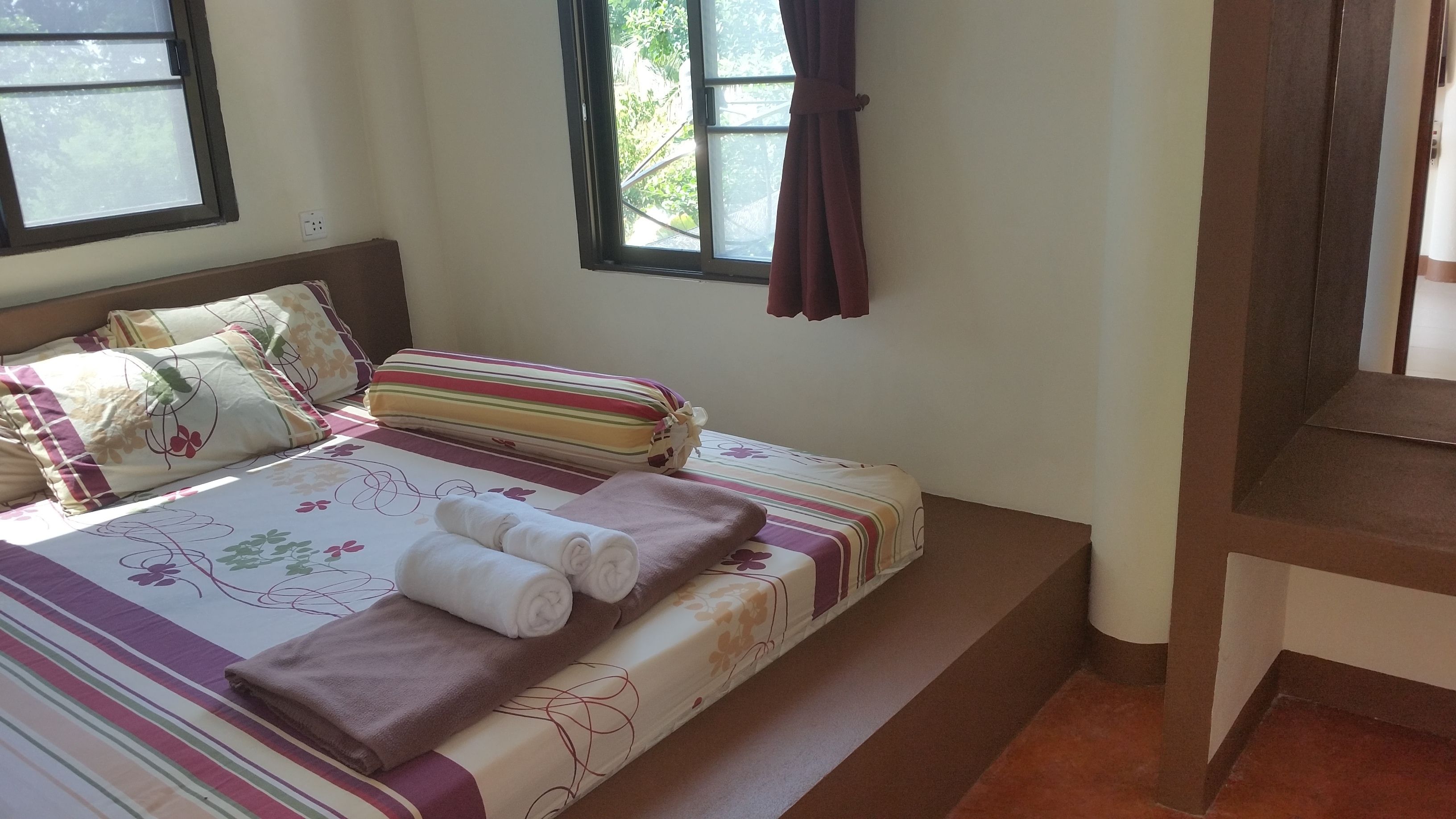 A neatly made bed with floral bedding, pillows, and a rolled towel.