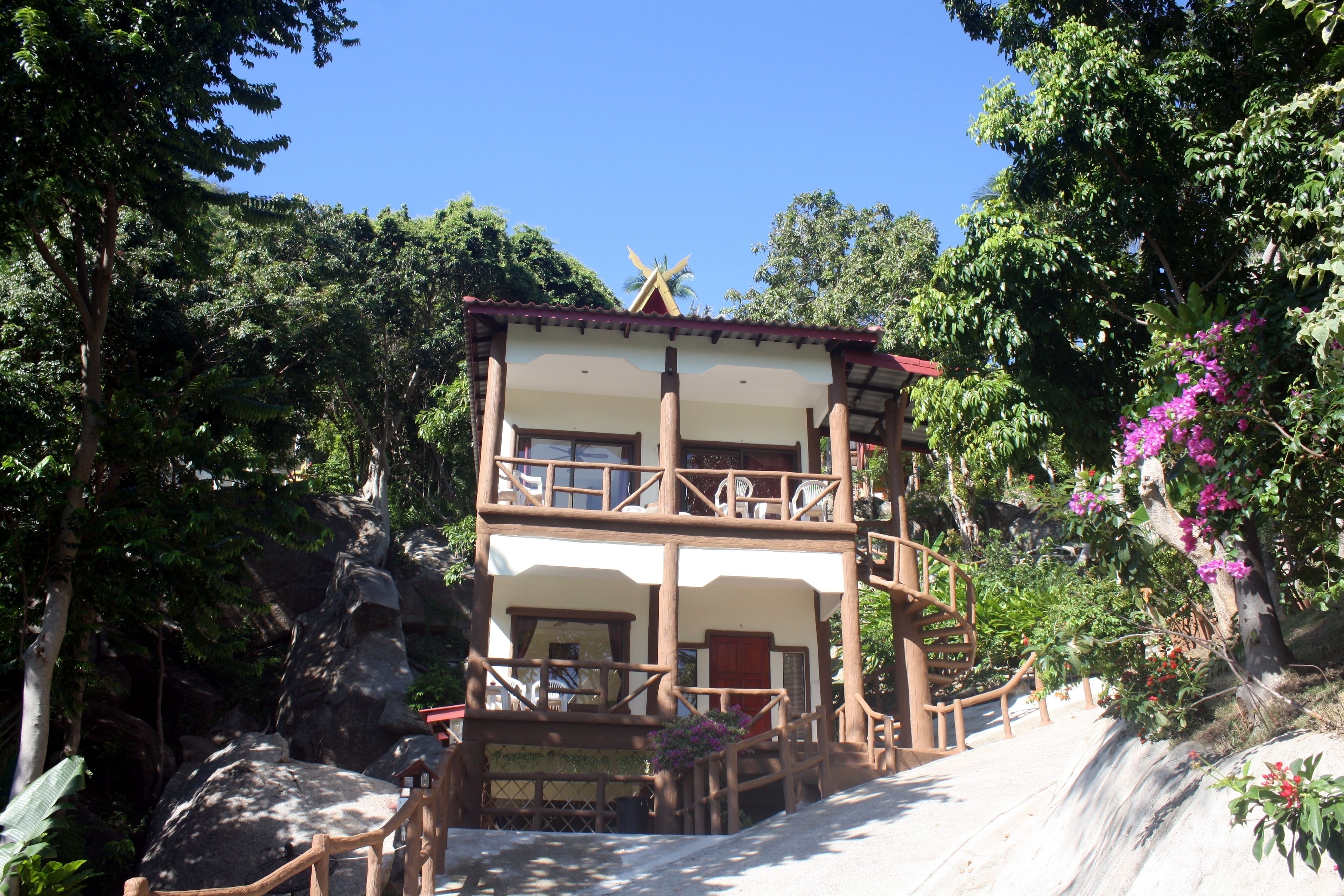 A two-story building with a balcony, surrounded by lush greenery and a waterfall.
