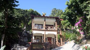 A two-story building with a balcony, surrounded by lush greenery and a waterfall.