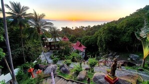 A tropical resort with a view of the ocean at sunset, featuring a traditional building with a red roof, lush greenery, and a statue. - Moonstone Studio (Ko Pha-ngan)