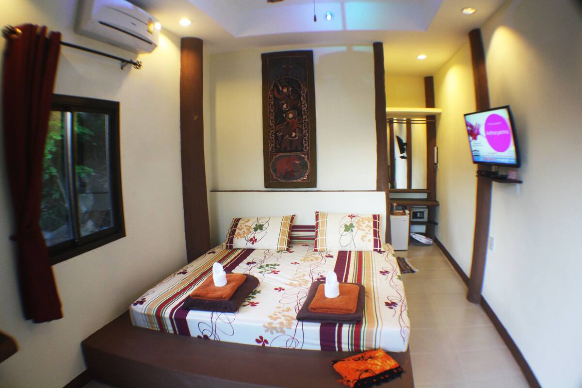 A hotel room with a bed, a television, and a window with curtains.
