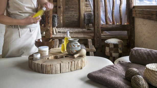 A rustic wooden interior with a person preparing a drink, wooden furniture, and a view of mountains through a window. - CGH Résidences & Spas Les Chalets d'Angèle (Chatel)