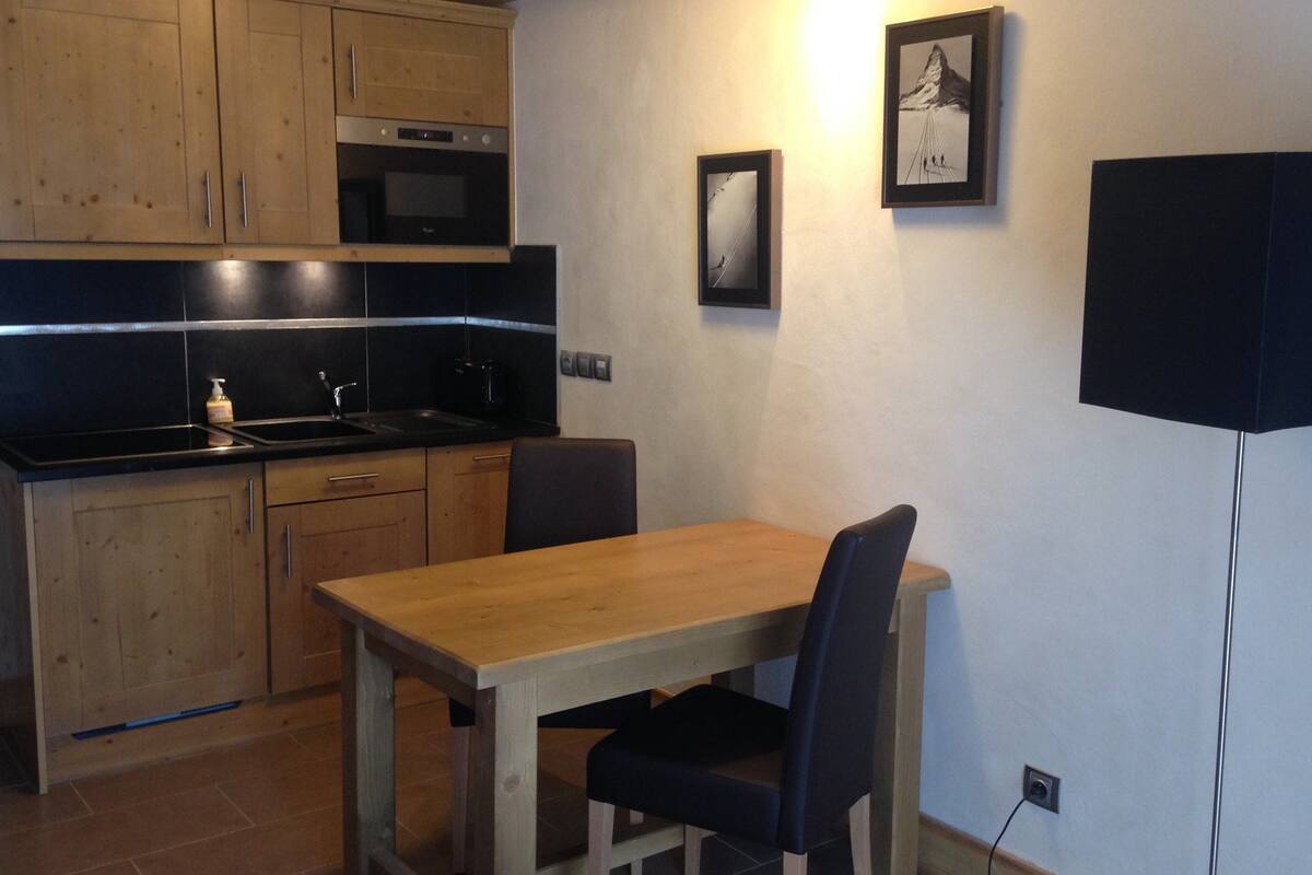 A compact kitchen with wooden cabinets, a black countertop, and a wooden dining table with two chairs.