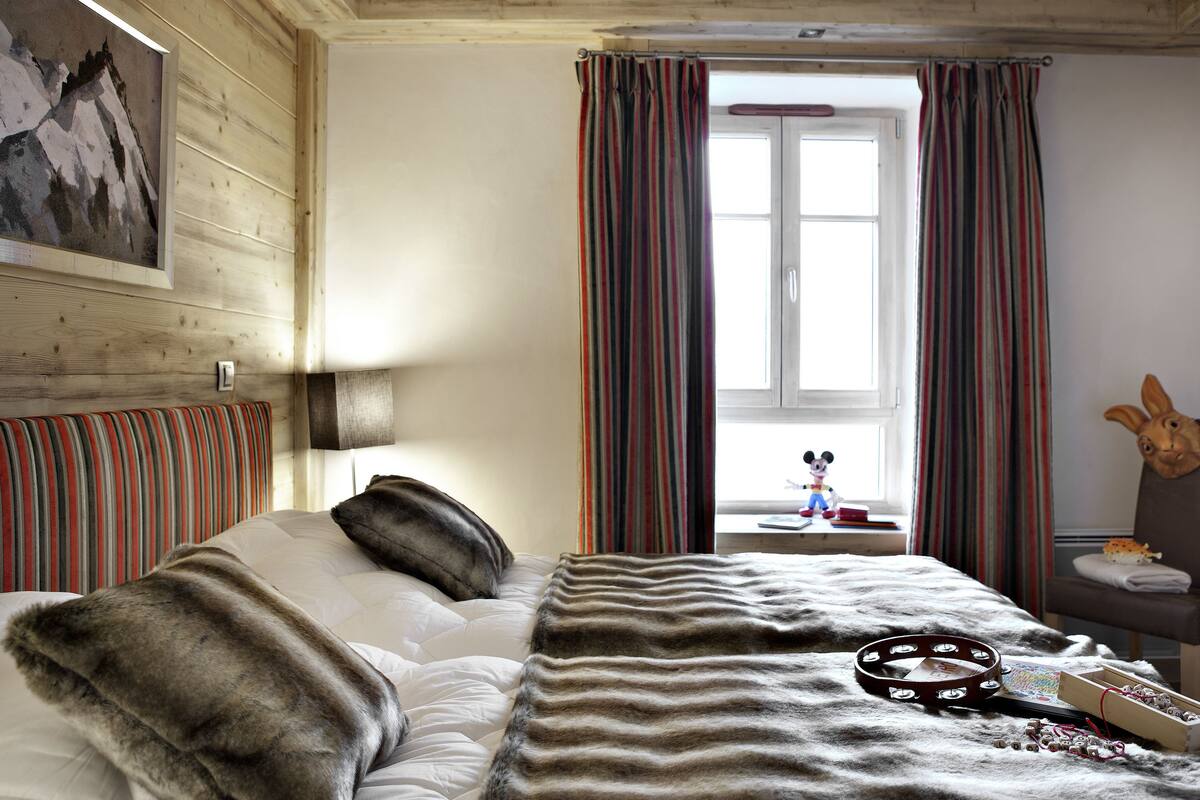 A hotel room with a bed, a window with curtains, a headboard, and a wall-mounted picture.