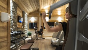 A gym with wooden walls, exercise equipment, and a person using a stationary bike. - CGH Résidences & Spas Les Chalets d'Angèle (Chatel)
