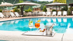 A poolside area with lounge chairs, umbrellas, and a bar area with drinks. - Hotel Ariston (Levico Terme)