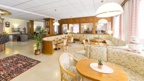 A spacious lobby with a central seating area, multiple tables, and a reception desk. - Hotel Ariston (Levico Terme)