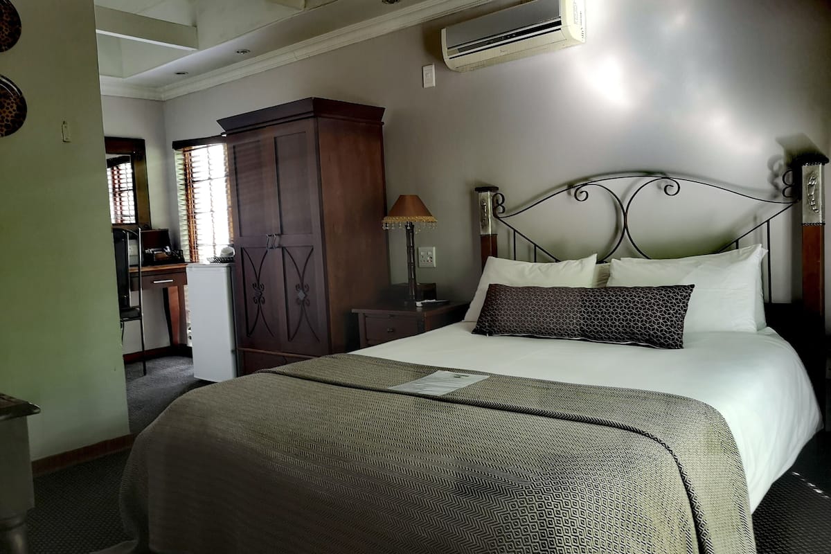 A bedroom with a bed, a wardrobe, a desk, and an air conditioning unit.
