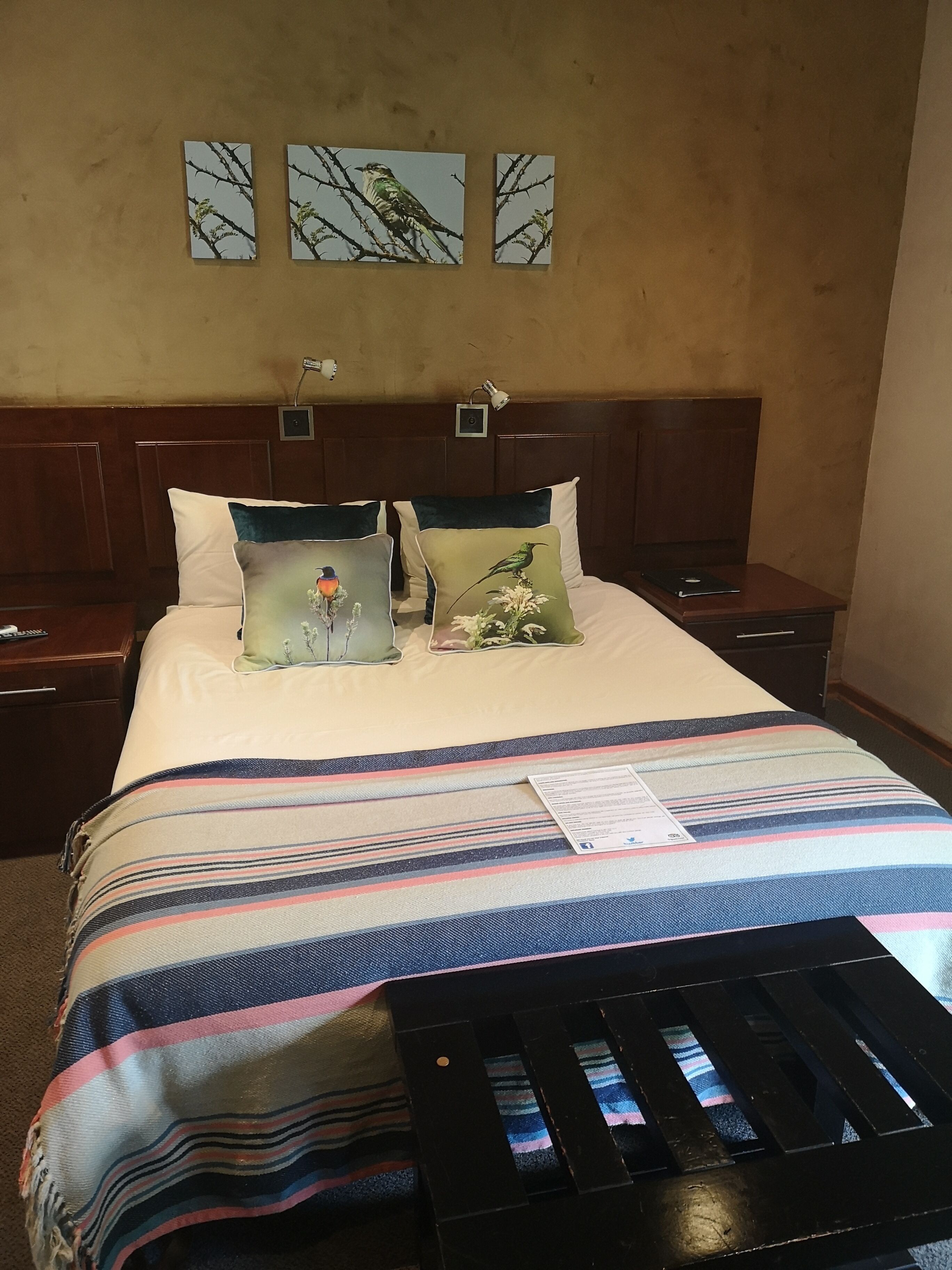 A hotel room with a bed, two nightstands, a wooden headboard, and three wall-mounted paintings of birds.