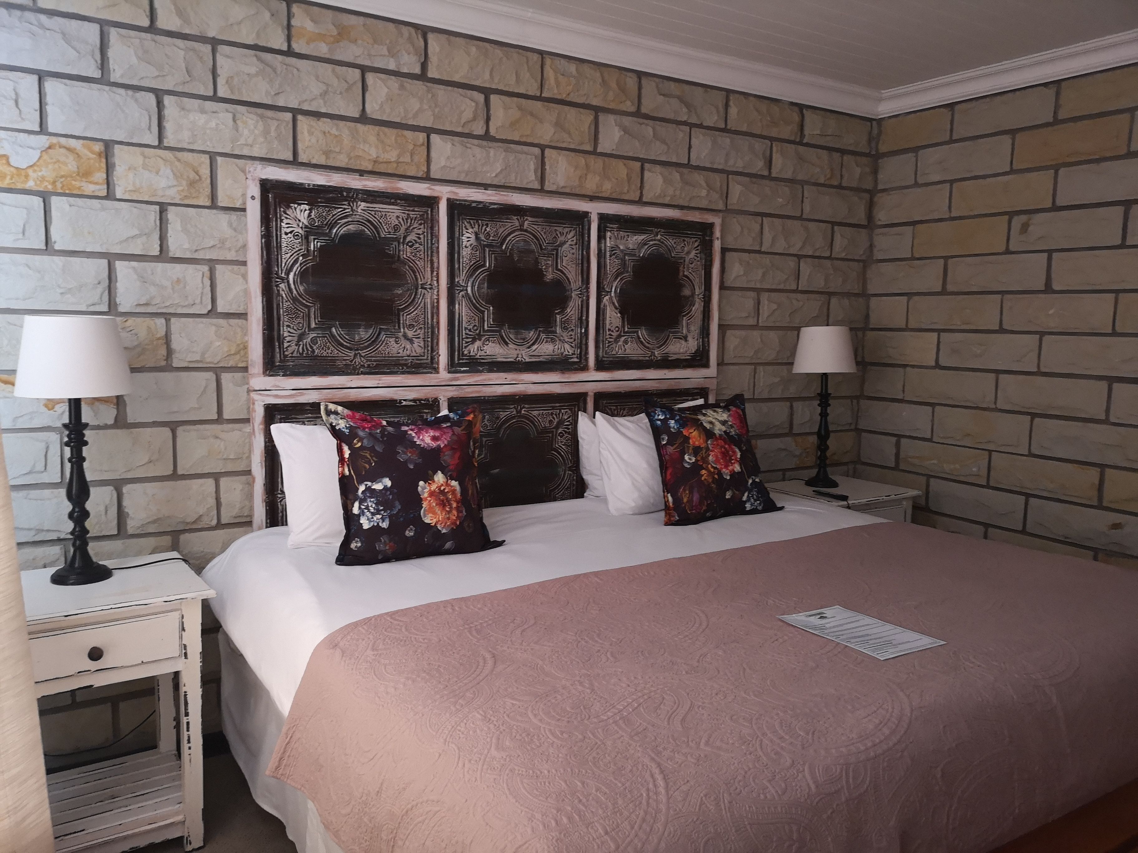 A bedroom with a stone wall, a bed with a floral pillow, and two bedside lamps.
