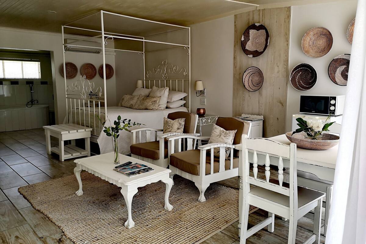 A cozy living room with a white sofa set, a coffee table, and a dining table. There are woven baskets and wall decor on the walls.