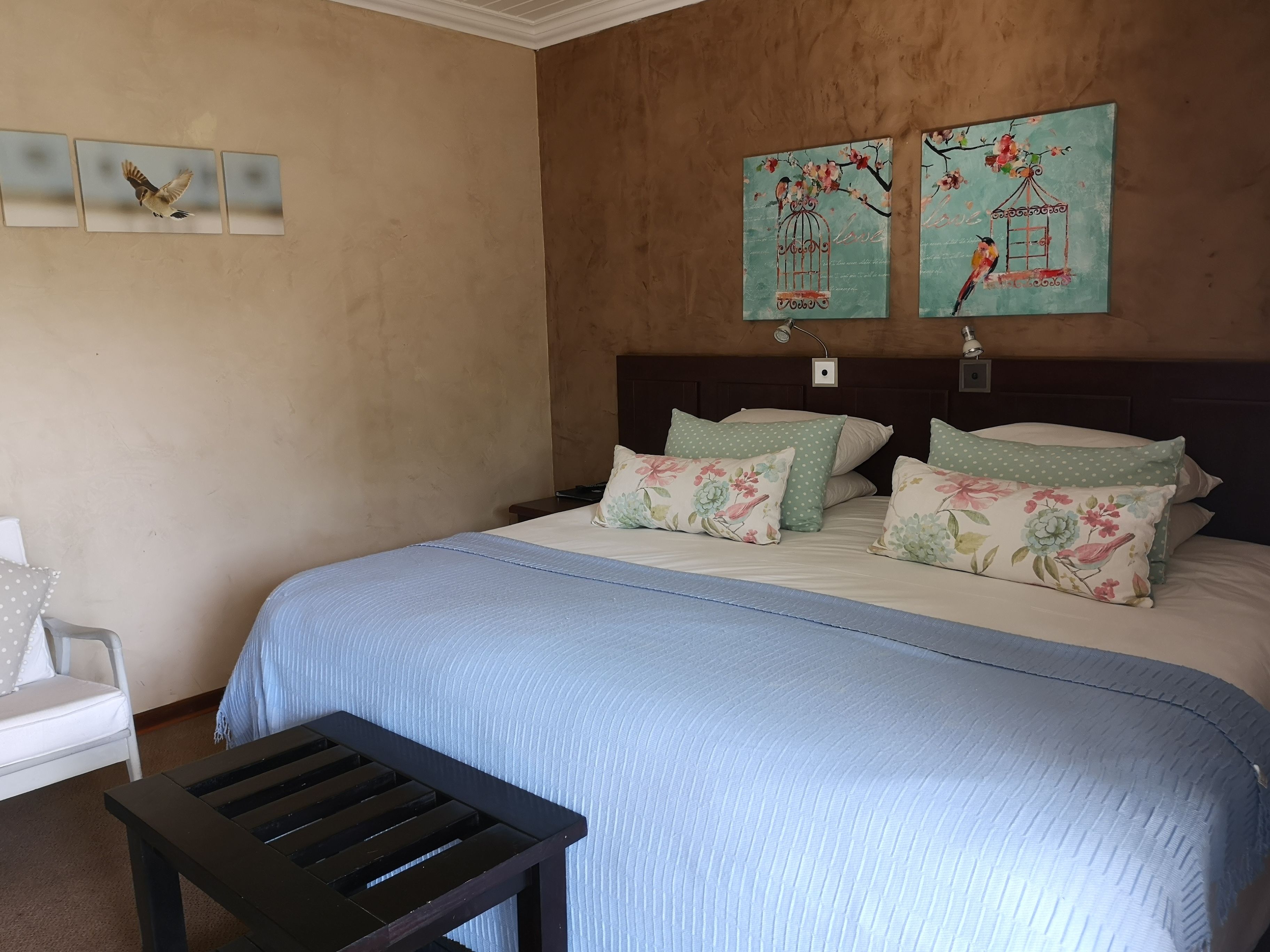 A bedroom with a bed, pillows, a nightstand, a wooden bench, and wall art.