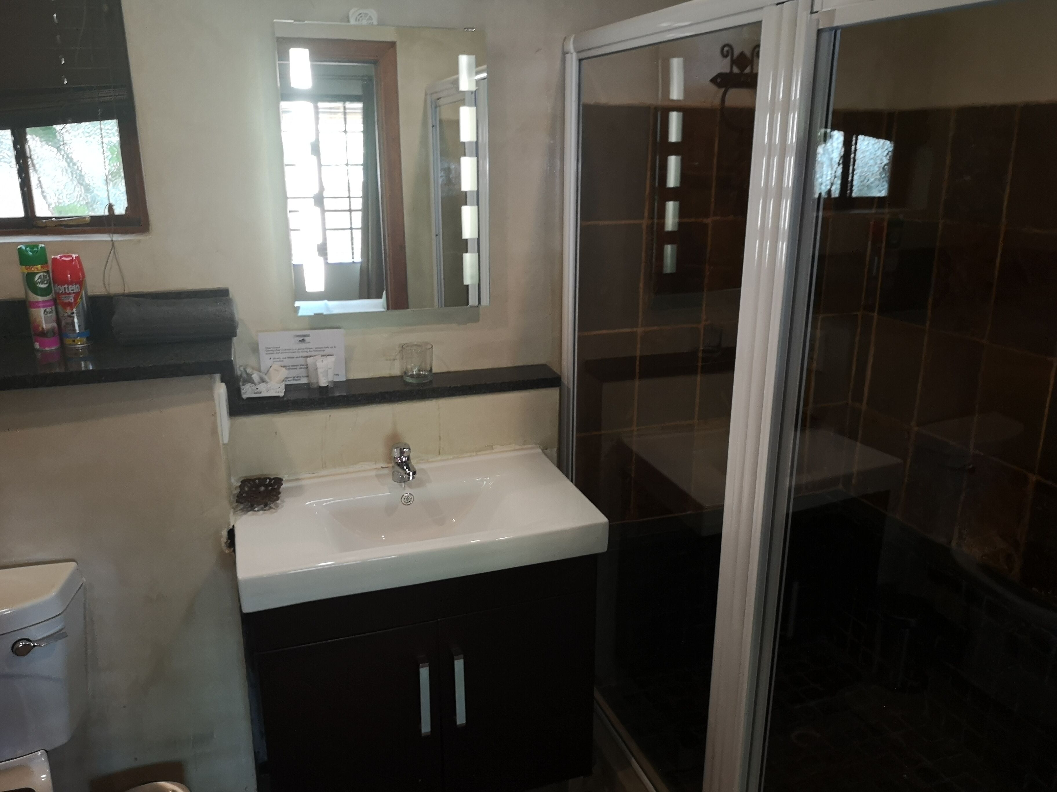 Un baño con lavamanos blanco, muebles oscuros, un espejo y cabina de ducha de vidrio.