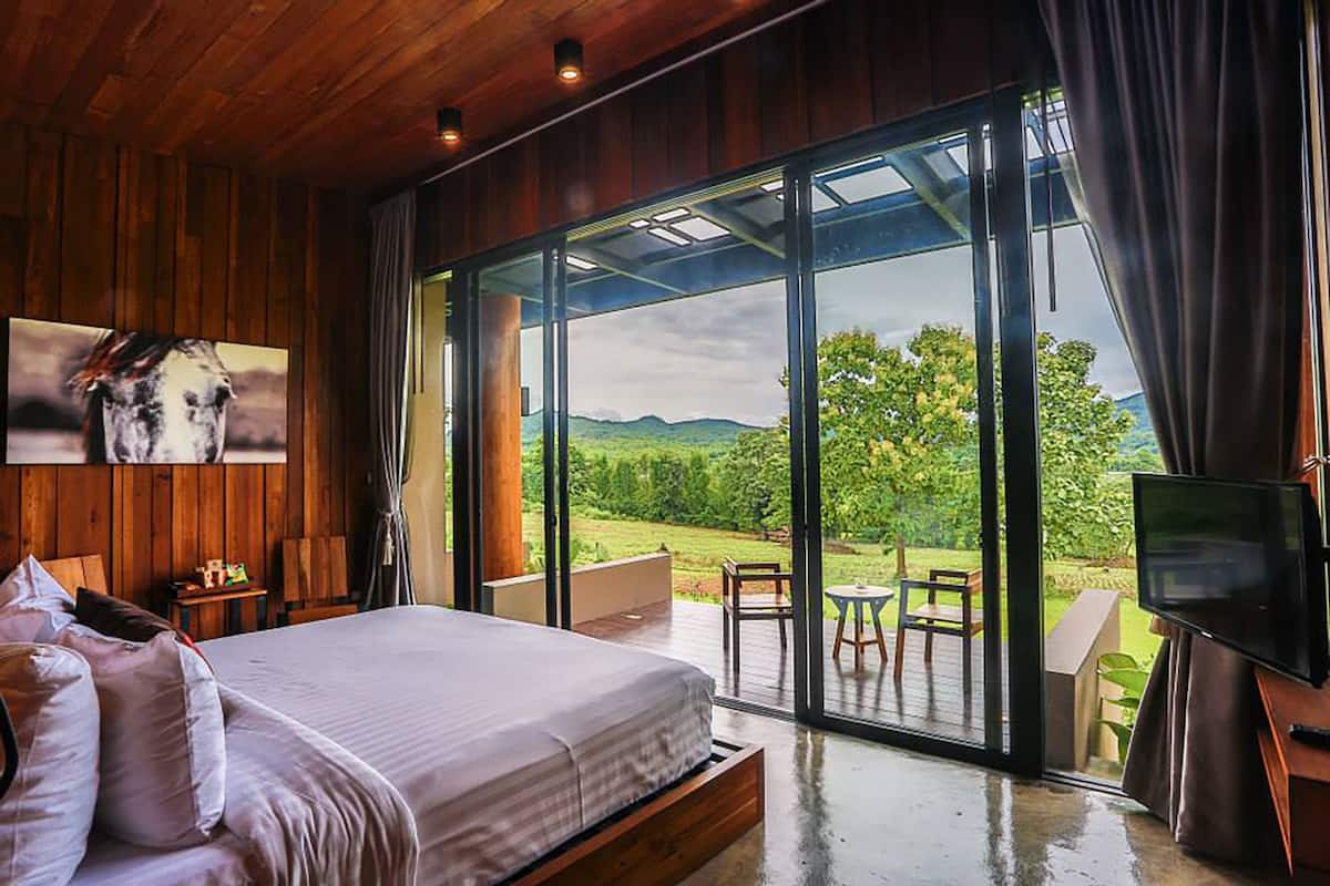 A bedroom with a large bed, a TV, and a sliding glass door leading to an outdoor patio with a view of the countryside.