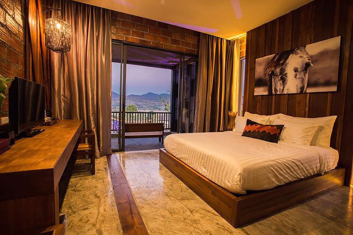 A bedroom with a large bed, a desk, and a view of the outdoors.