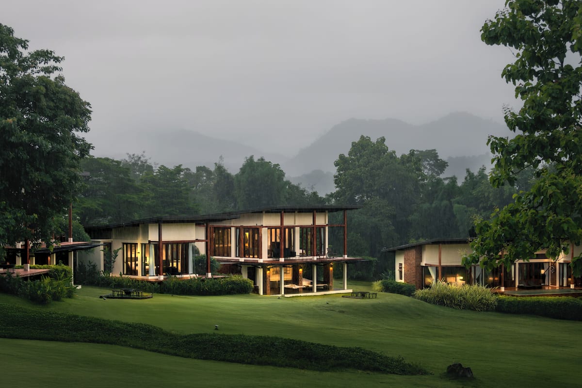 A modern house with large windows, a well-maintained lawn, and a view of mountains in the background.