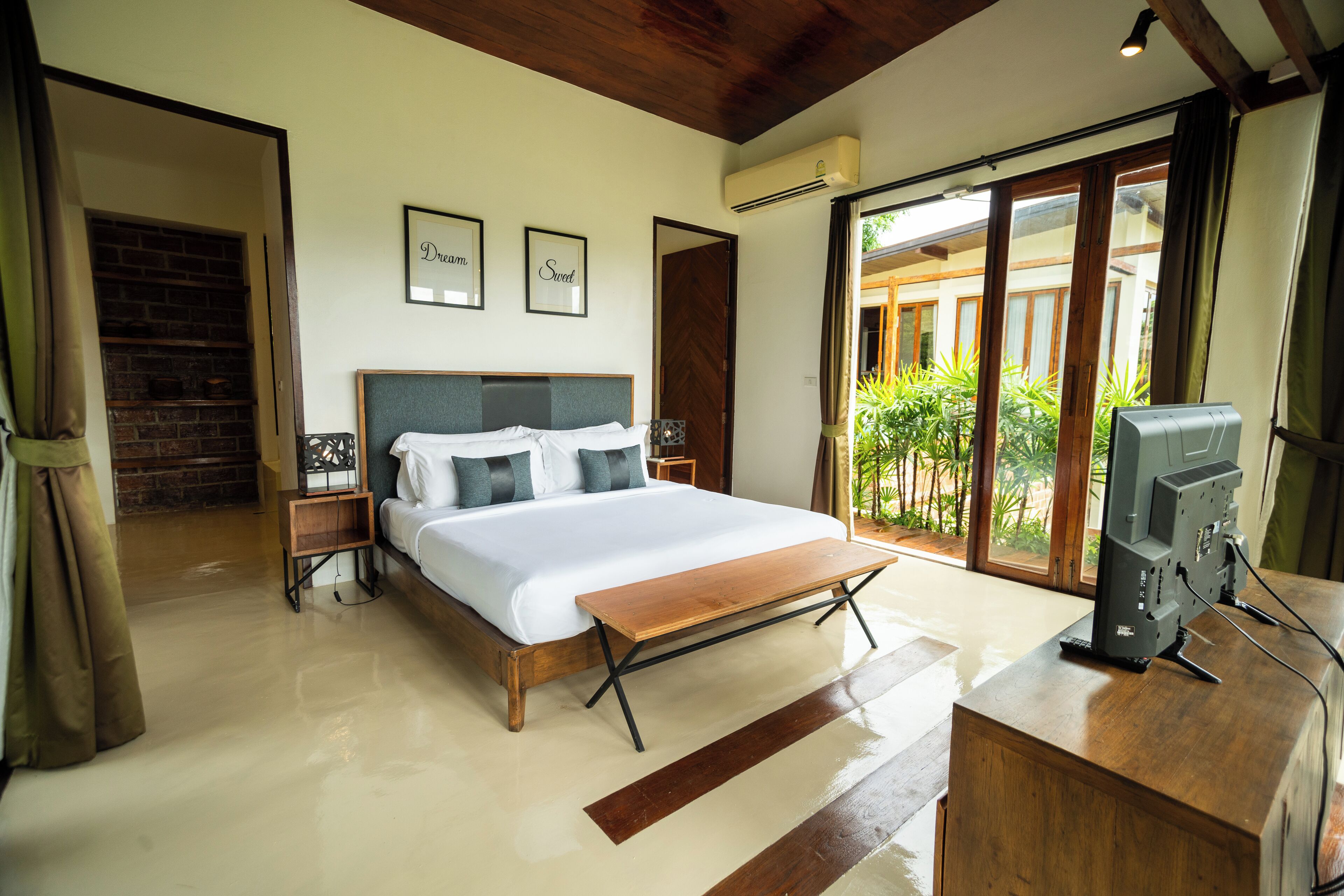A bedroom with a large bed, a wooden bench, a TV, and a view of the outdoors.