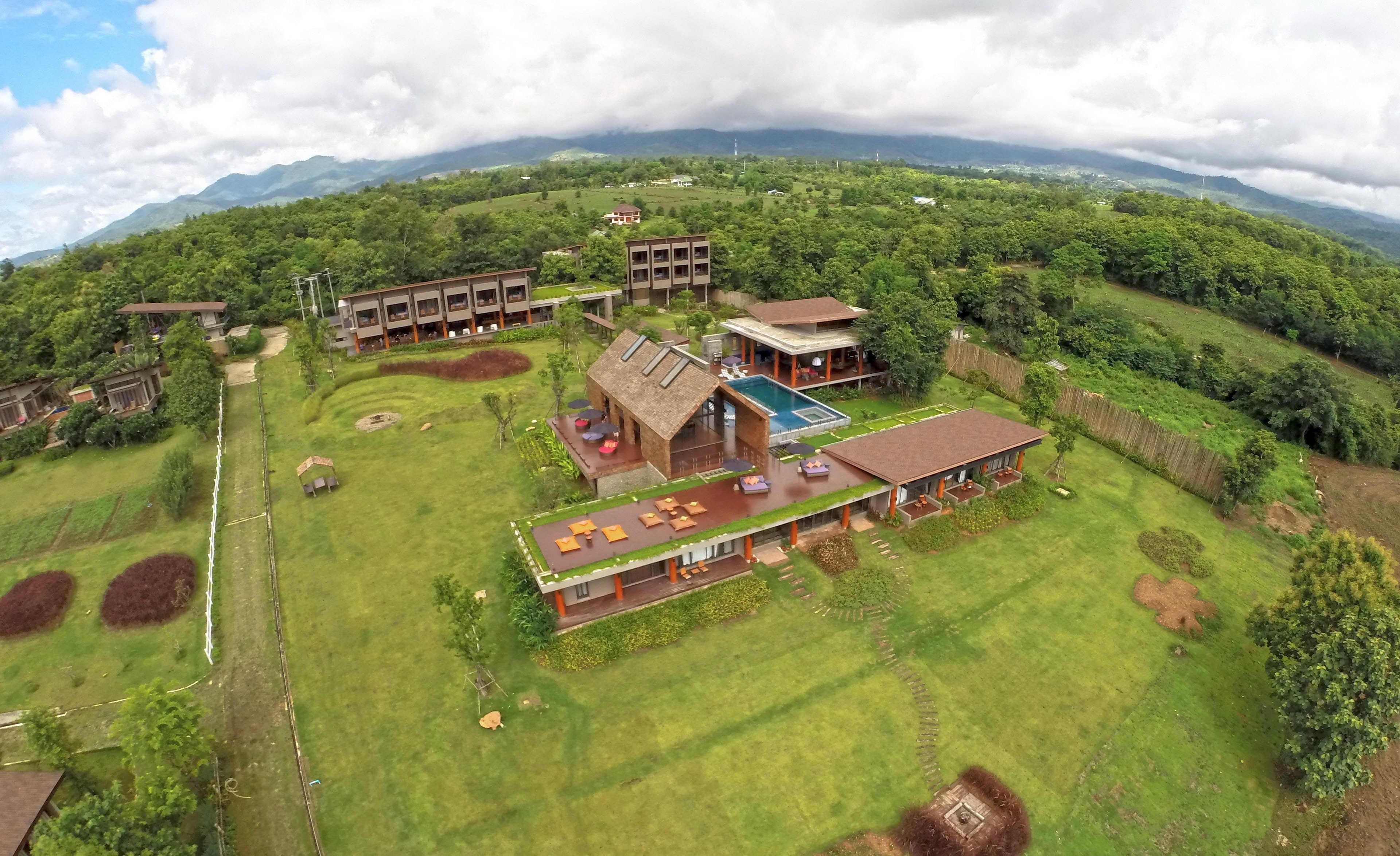 Vista aérea de un complejo turístico con varias edificaciones, piscina y exuberante vegetación.