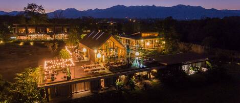 A hotel with multiple buildings connected by walkways, outdoor seating areas, and a view of mountains in the background.