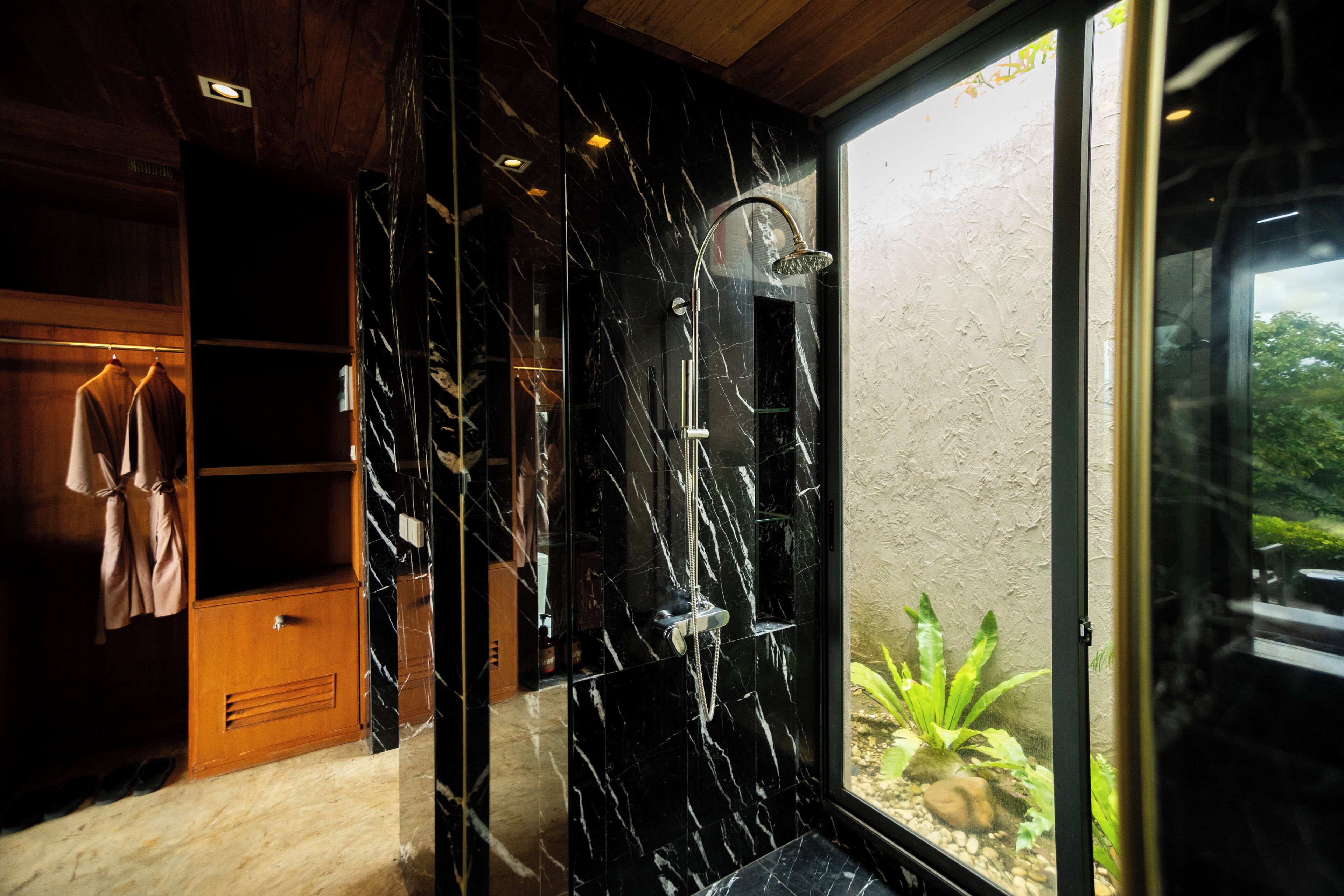 A modern bathroom with a shower, marble walls, and a view of greenery outside.