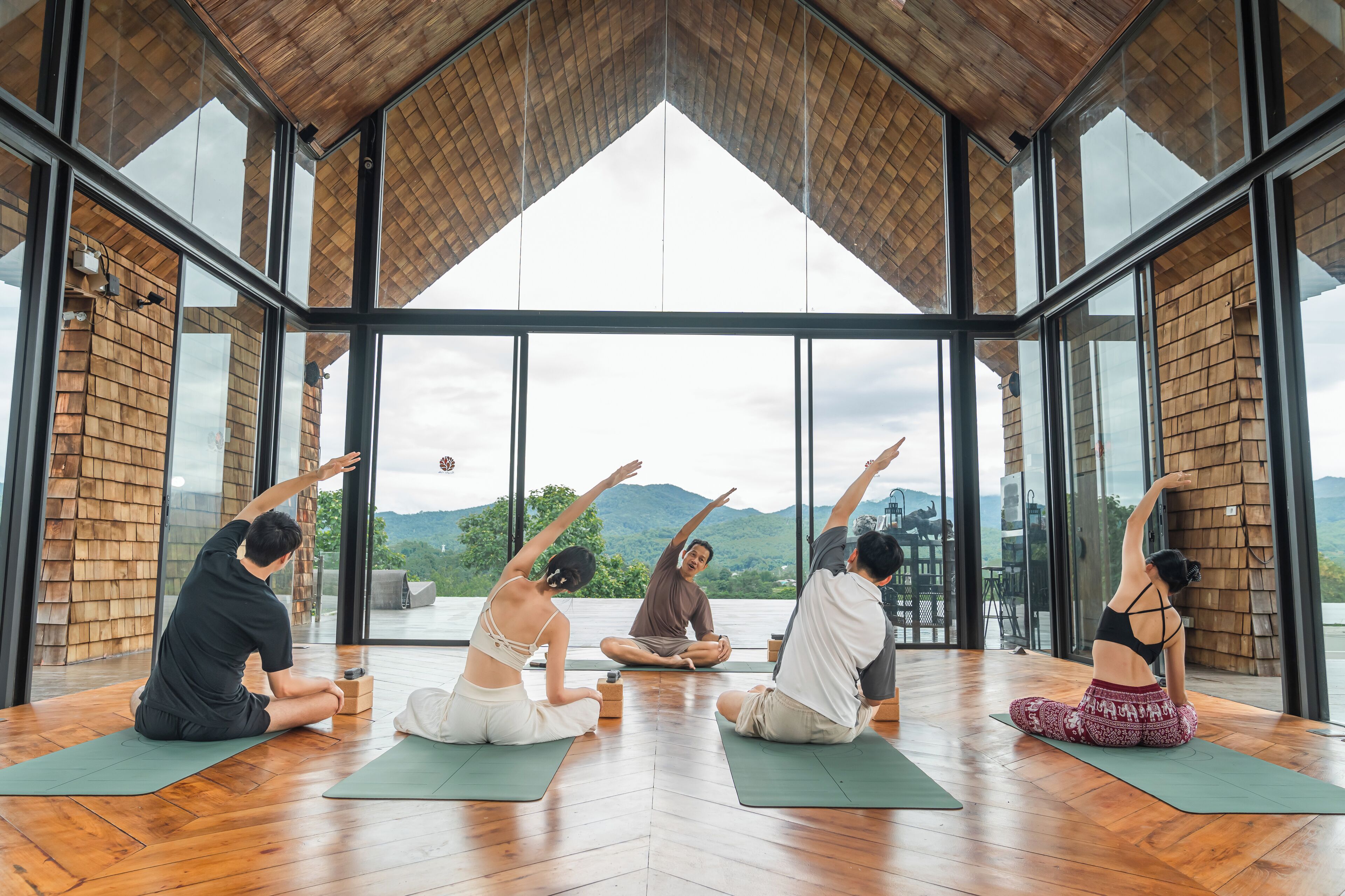 A group of people practicing yoga in a spacious room with large windows and a wooden ceiling.