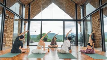 A group of people practicing yoga in a spacious room with large windows and a wooden ceiling.