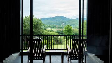 Un balcón con dos sillas y una mesa de madera, con vista a un paisaje verde exuberante y montañas a lo lejos.