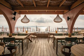 An outdoor dining area with wooden tables and chairs, a view of the sea, and hanging wicker lamps. - Van der Valk Hotel Saint Aygulf (Fréjus)