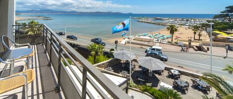 Un balcon avec coin salon extérieur donnant sur une plage et un port de plaisance.