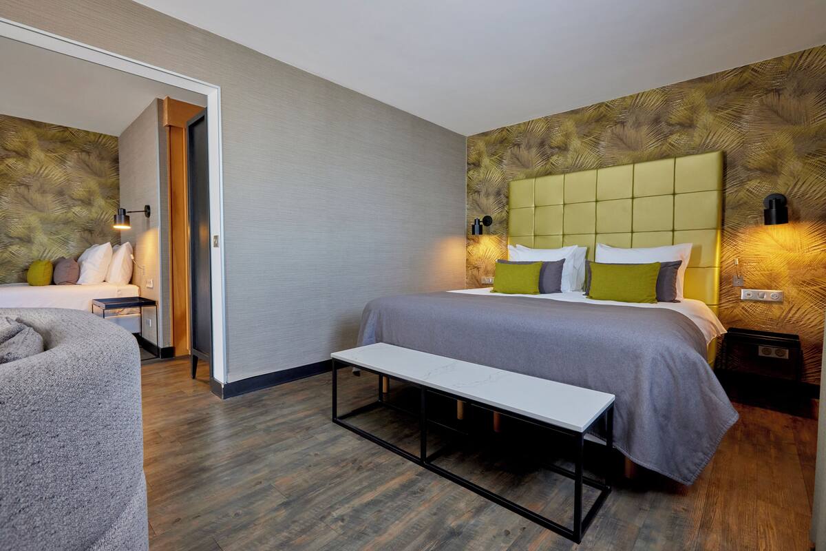 Une chambre d’hôtel moderne avec un grand lit, des tables de chevet, un banc et un petit coin salon.